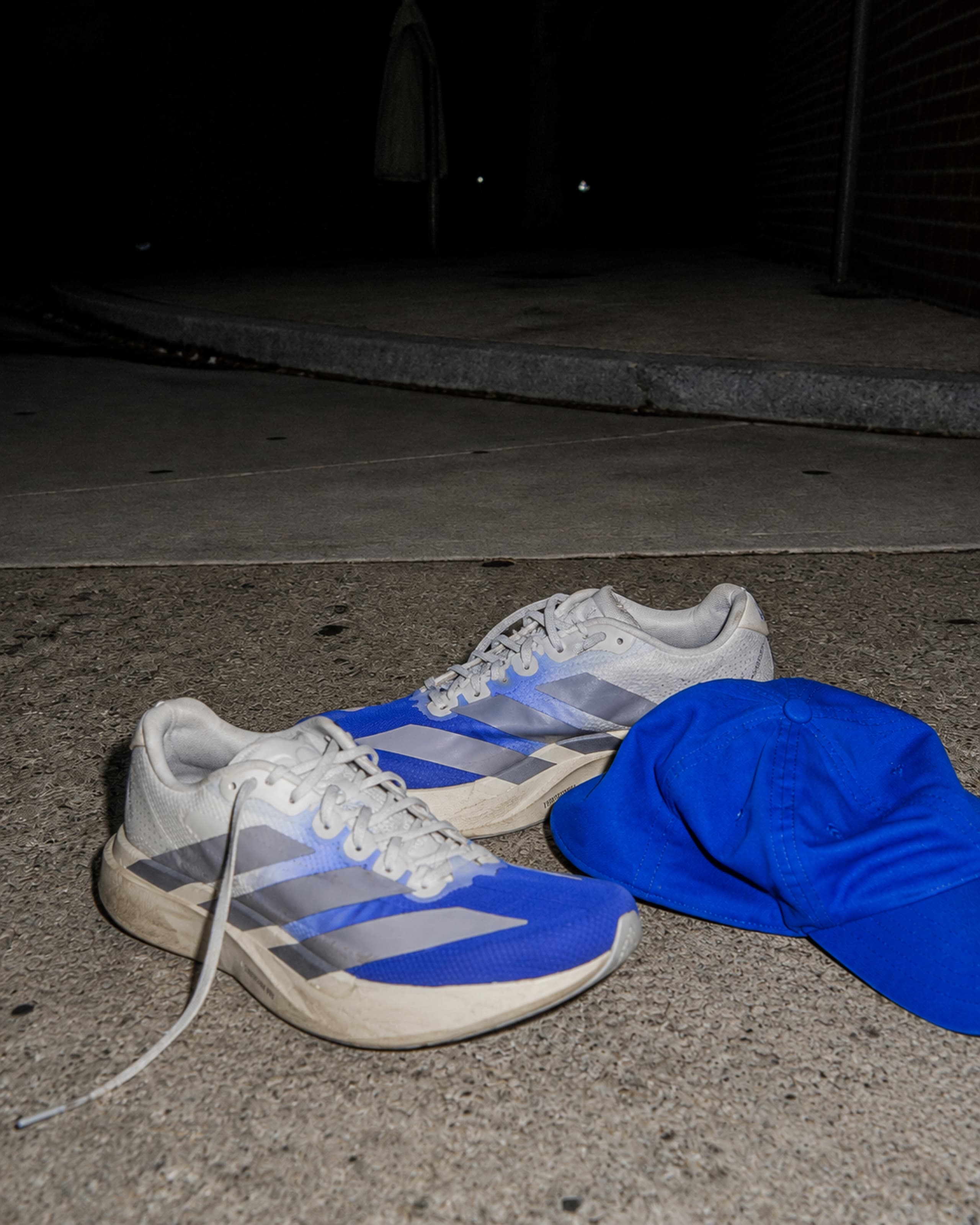 Running shoes and a cobalt cap left on the pavement at night.