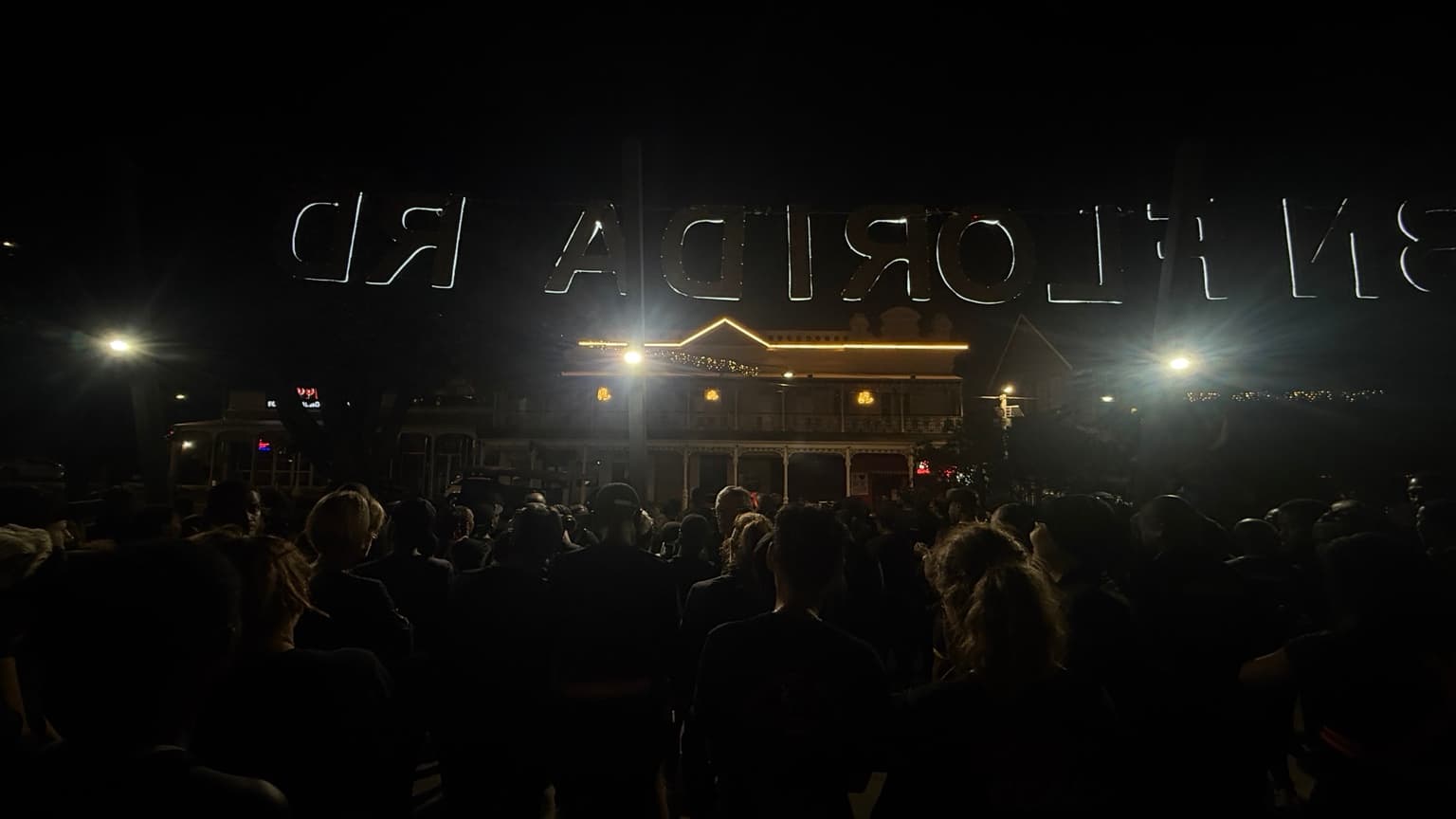 A crowd gathered outdoors at night facing a building outlined with lights.