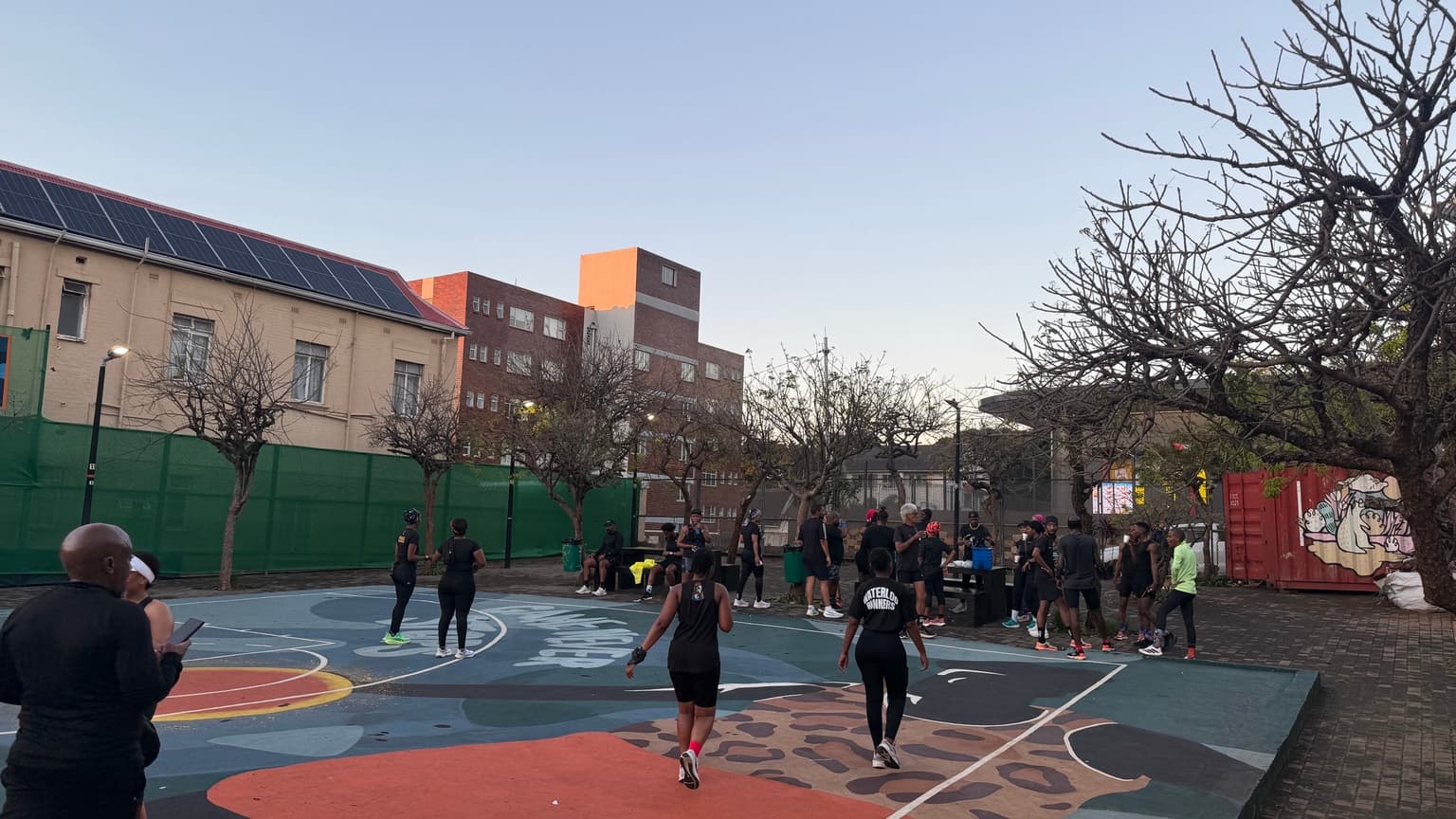 Runners gathering on a painted outdoor court beside trees and buildings.